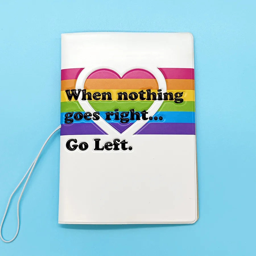A white PVC passport cover featuring a rainbow heart design with the text When nothing goes right Go Left.