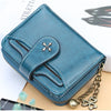 A teal PU leather compact wallet with a zipper and gold chain resting on a light background.