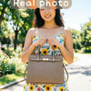 A woman holds a brown genuine leather shoulder bag outdoors in a park setting.