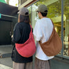 A person wearing a black shirt and a grey cap holds a reddish-pink corduroy casual crossbody bag in front of a glass door.