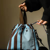 A person is holding an insulated lunch bag with brown straps and blue and brown stripes against a neutral background.