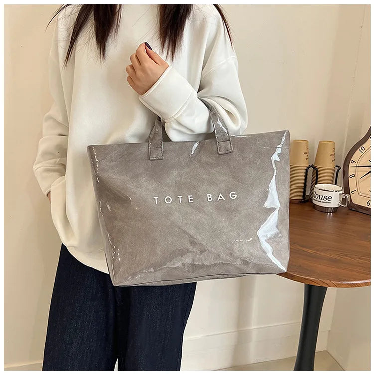 A person holds a gray transparent waterproof PVC tote bag against a light background.