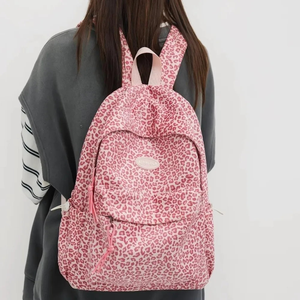 A pink leopard print laptop backpack with padded straps carried by a person.