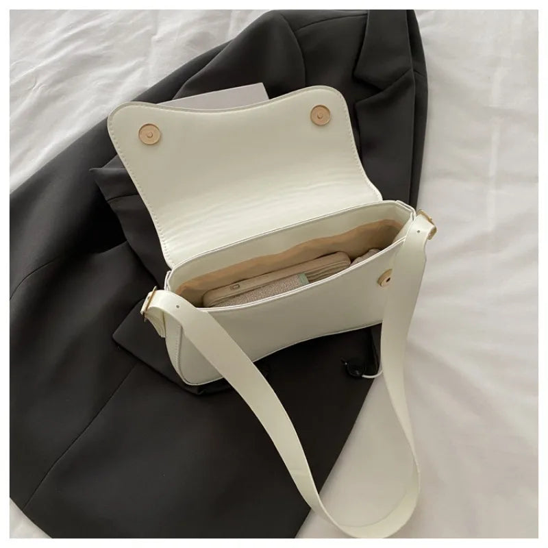 A white vintage curved flap shoulder bag with light tan lining rests on a dark gray fabric.