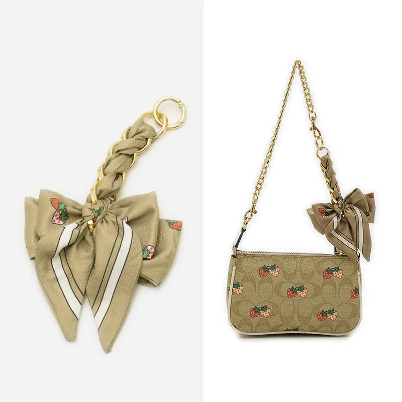 A beige adjustable bag strap with a gold-tone chain and a fabric pouch featuring a repeating pattern of small fruit motifs.