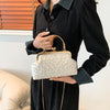 A woman holds a light cream pearl embellished crossbody shoulder bag against a dark sweater.