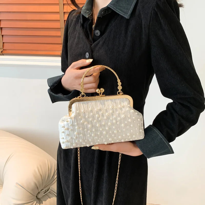 A woman holds a light cream pearl embellished crossbody shoulder bag against a dark sweater.