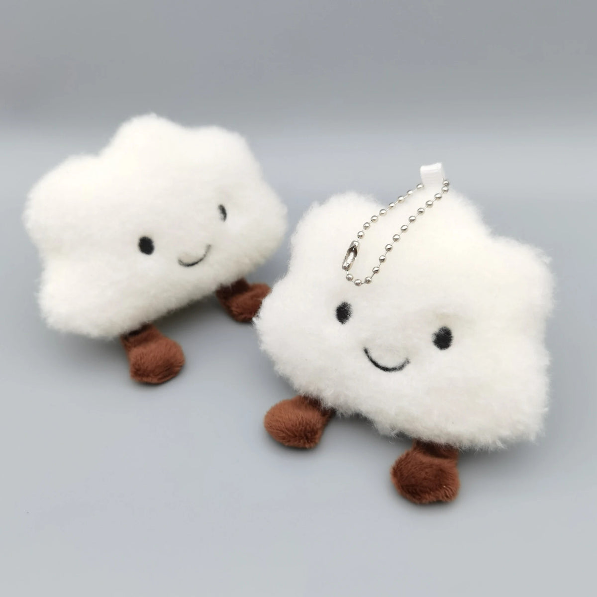 A white fluffy cloud shaped plush toy with brown feet and a silver chain attached for a keychain.