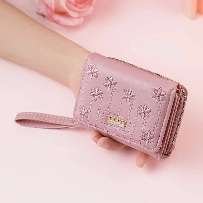 A pink PU leather women's wallet with a zipper closure and decorative floral stitching is held by a hand.