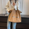 A woman wearing a cream sweater holds a brown canvas tote bag with the text TOTE BAG.