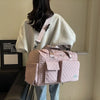 A person is holding a pink quilted portable travel duffle bag against a light wall.