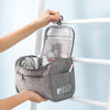 A gray portable toiletry bag is hanging on a white railing, showing its interior compartments.