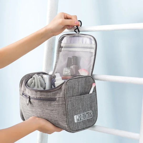 A gray portable toiletry bag is hanging on a white railing, showing its interior compartments.