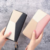 A hand holds a fashion zipper wallet featuring a geometric design in beige, black, and pink tones.