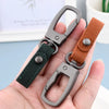 A close-up of a genuine leather keyring keychain with a dark green strap and a gray metal clasp being held in a hand.