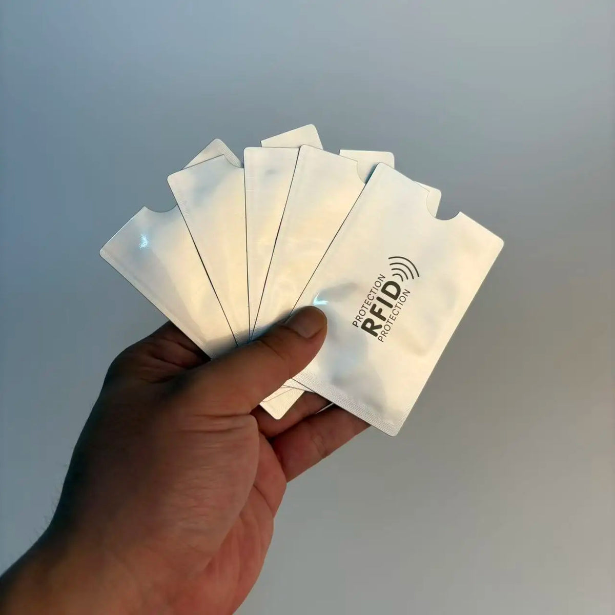 A hand holds a stack of five white RFID blocking card sleeves against a light gray background.