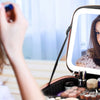 A woman applies makeup using an LED lighted train case with adjustable dividers.