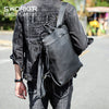 A person wearing a dark denim jacket and jeans carrying a black full-grain leather backpack.