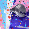 A close-up of colorful, shiny birthday party gift bags in pink, blue, and purple packaging.