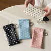 A hand holds a white polka dot eyeglass pouch with a keychain on a white table.