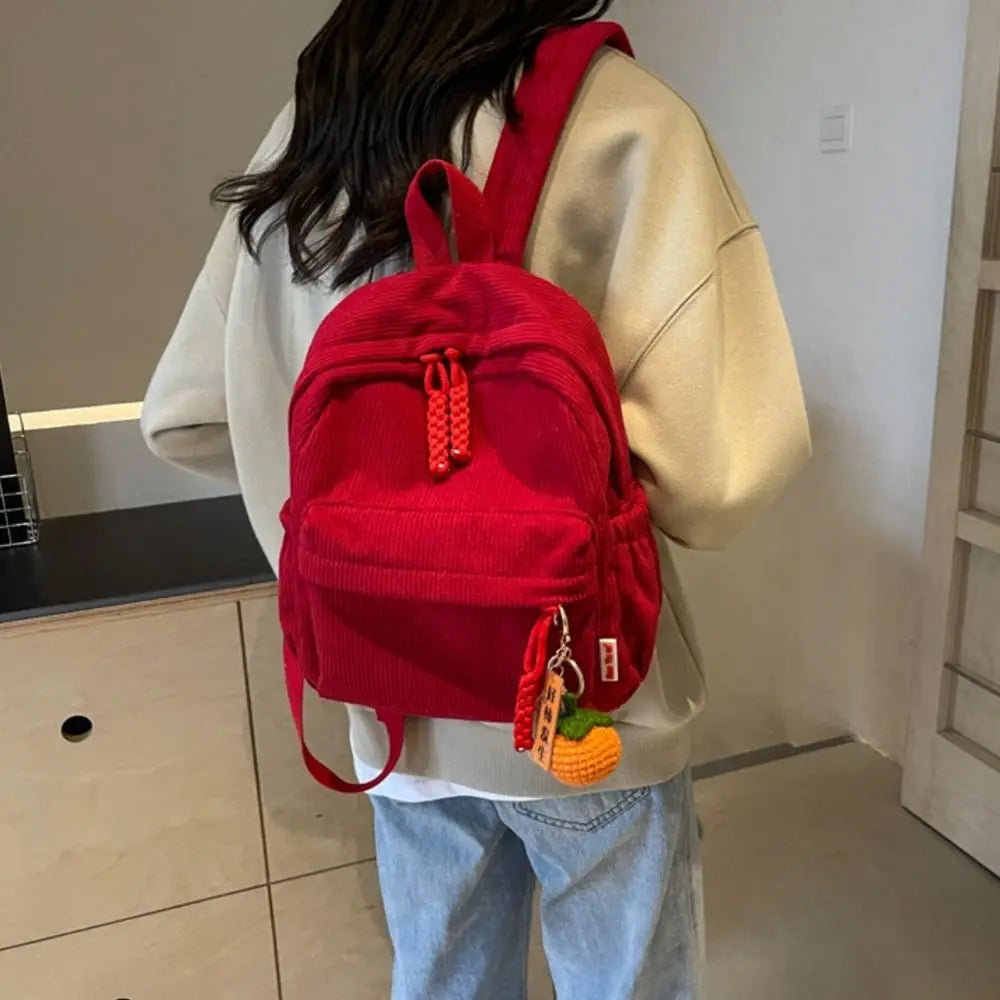 A person is wearing a bright red lightweight corduroy daily backpack over a cream-colored sweater.