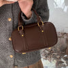 A brown vintage PU leather shoulder bag is held by a person wearing a gray sweater and plaid skirt.
