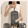 A person holds a gray waterproof hanging toiletry bag with various grooming tools inside, displayed on a white surface.