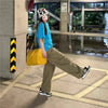 A person wearing a blue shirt and khaki pants is standing in an outdoor area holding a yellow faux crocodile tote bag.