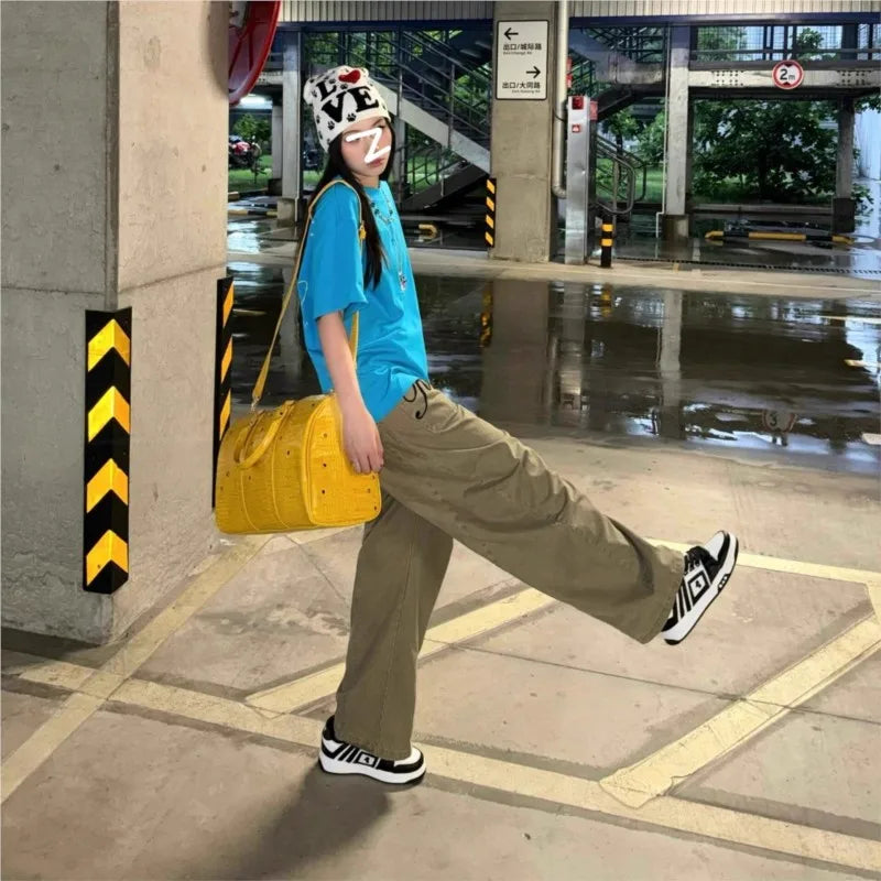 A person wearing a blue shirt and khaki pants is standing in an outdoor area holding a yellow faux crocodile tote bag.