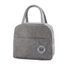 A gray insulated lunch bag with a woven strap and a circular logo on the front.