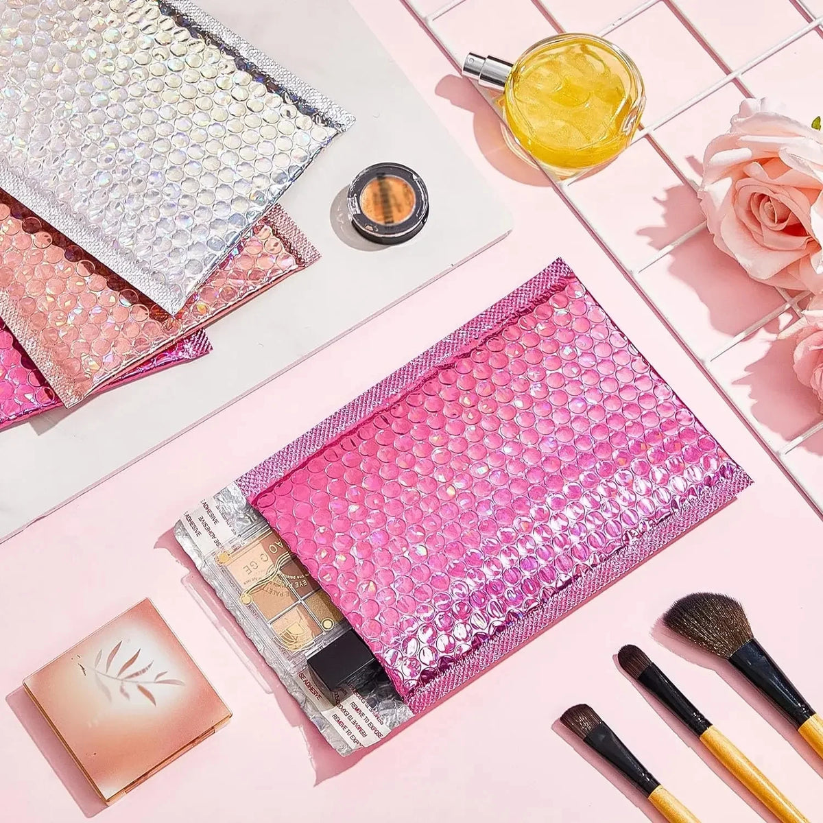 Pink holographic bubble mailers with self-seal closure and a gold liquid in a glass.