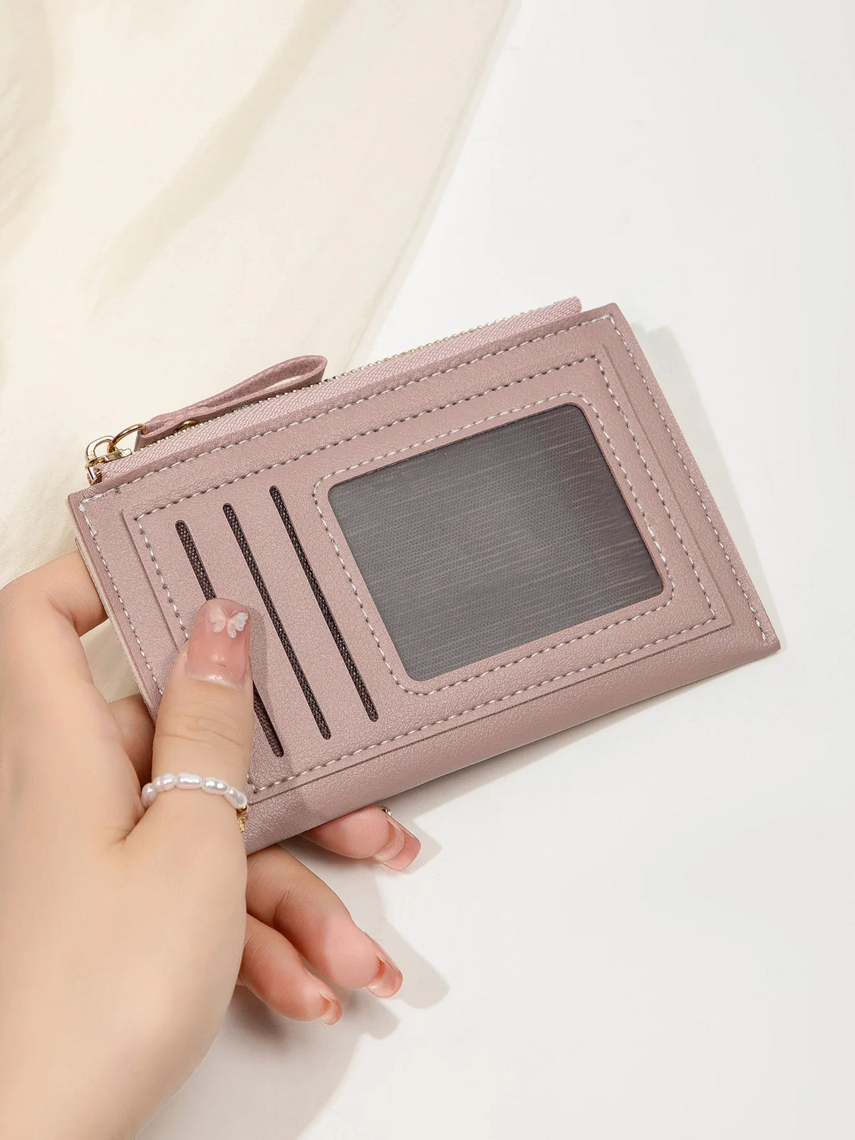 Une main tient un portefeuille en cuir PU rose pâle minimaliste avec une fenêtre en plastique transparent.