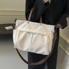 A beige lightweight nylon tote bag with multiple pockets carried by a person in a black blazer.