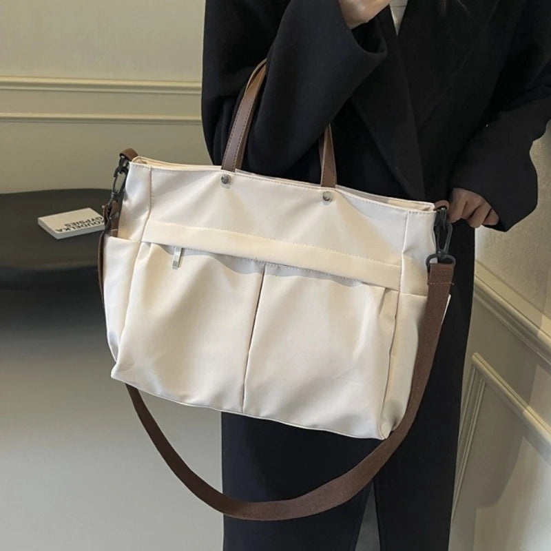 A beige lightweight nylon tote bag with multiple pockets carried by a person in a black blazer.
