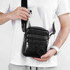 A hand holds a black vintage leather messenger bag against a white t-shirt.