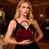 A woman holds a glossy burgundy evening handbag in a black dress at an event.