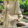 A woman wearing a light beige dress holds a cream embroidered crossbody shoulder bag in an outdoor setting.