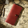 A reddish-brown genuine leather long bi-fold wallet with a snap closure resting on an old map.