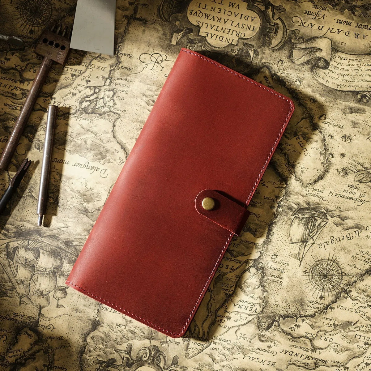 A reddish-brown genuine leather long bi-fold wallet with a snap closure resting on an old map.