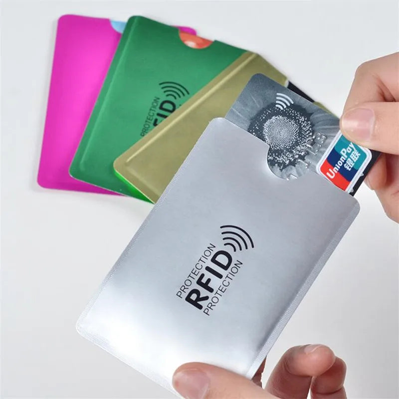 A hand holds a silver RFID protection card holder next to several colored cards.