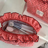 A red and white checkered makeup pouch with lace trim is open, showing makeup brushes inside.