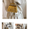A gold square crossbody bag with a chain strap is shown hanging from a sleeve of a light gray sweater.