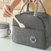 A hand is holding a white utensil inside a gray insulated lunch bag with fabric handles.
