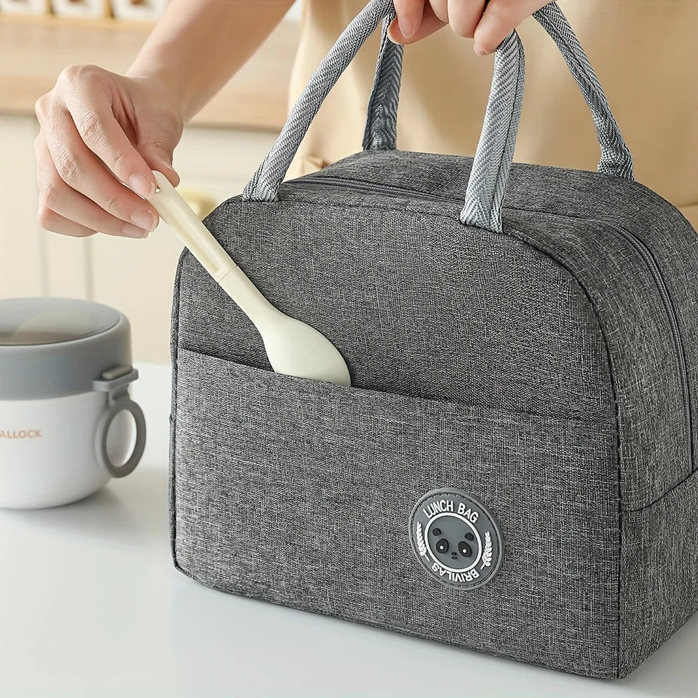 A hand is holding a white utensil inside a gray insulated lunch bag with fabric handles.