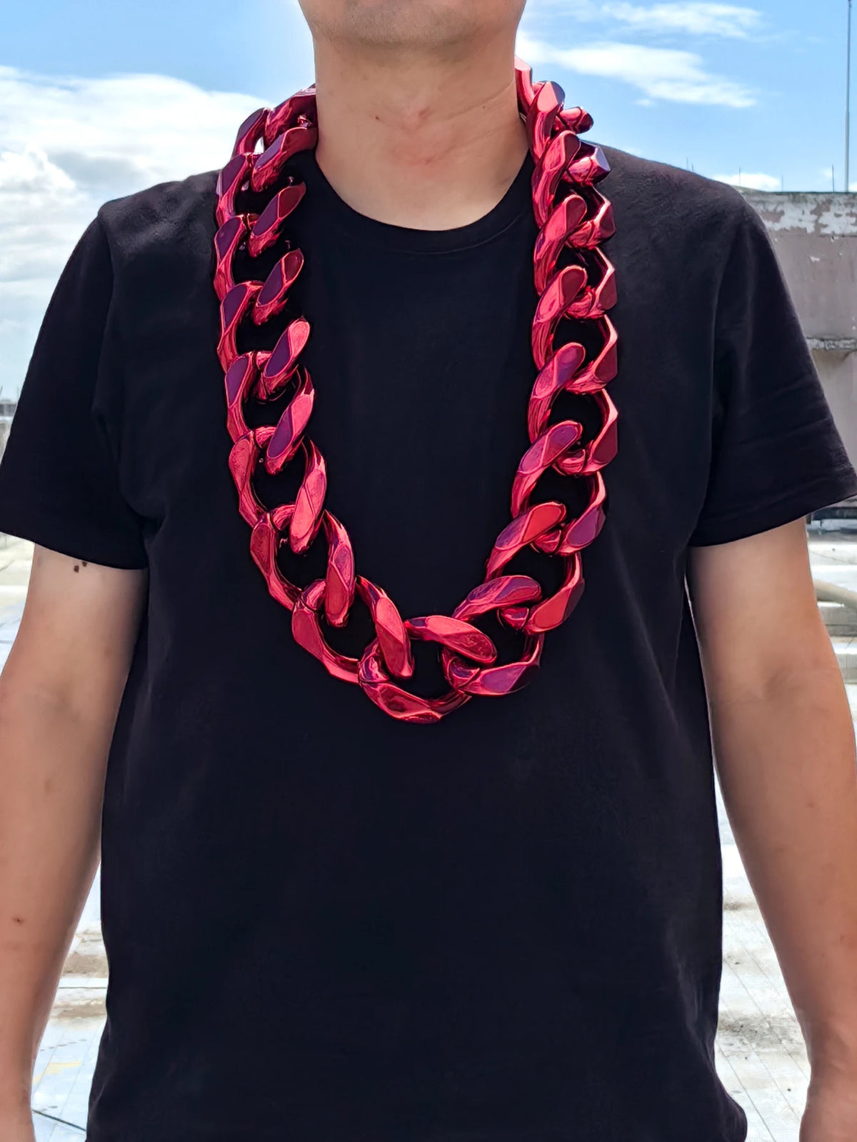 A man wearing a black t-shirt and a chunky red acrylic Cuban link necklace.