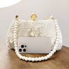 A white embroidered pearl chain clutch bag with a clear phone case resting on it.