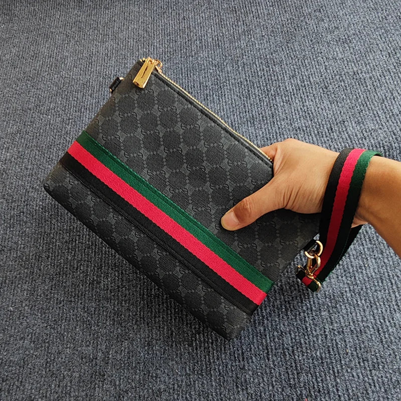 Eine schwarz-rote gestreifte Clutchtasche mit goldener Reißverschluss und grünem Riemen wird von einer Hand gehalten.