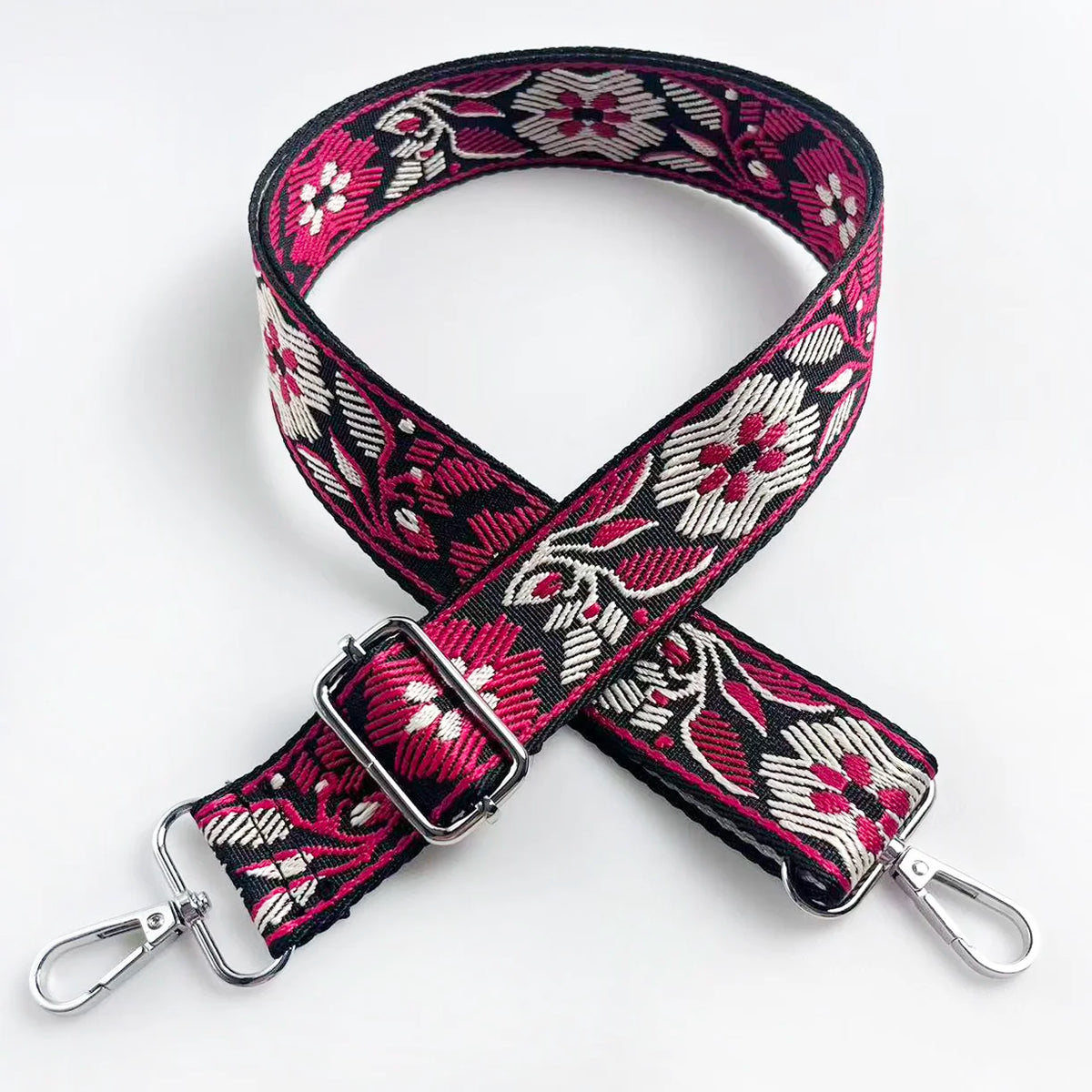A black and pink floral patterned fabric strap for a crossbody bag, featuring a silver buckle.