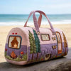 A quilted lavender travel duffle bag with pink handles and embroidered nature scenes sits on a wooden surface.