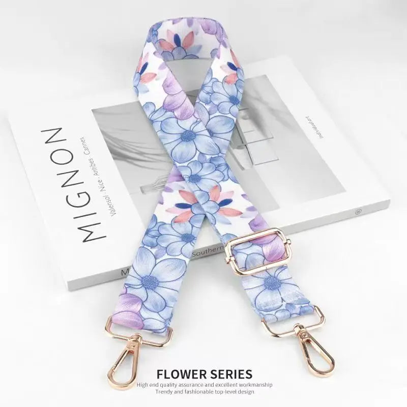 A floral patterned nylon bag strap in purple and blue is displayed on a white box.